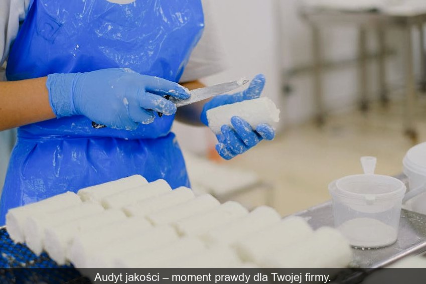 Audytor w białym kitlu z clipboardem weryfikuje procesy w nowoczesnym zakładzie produkującym żywność.